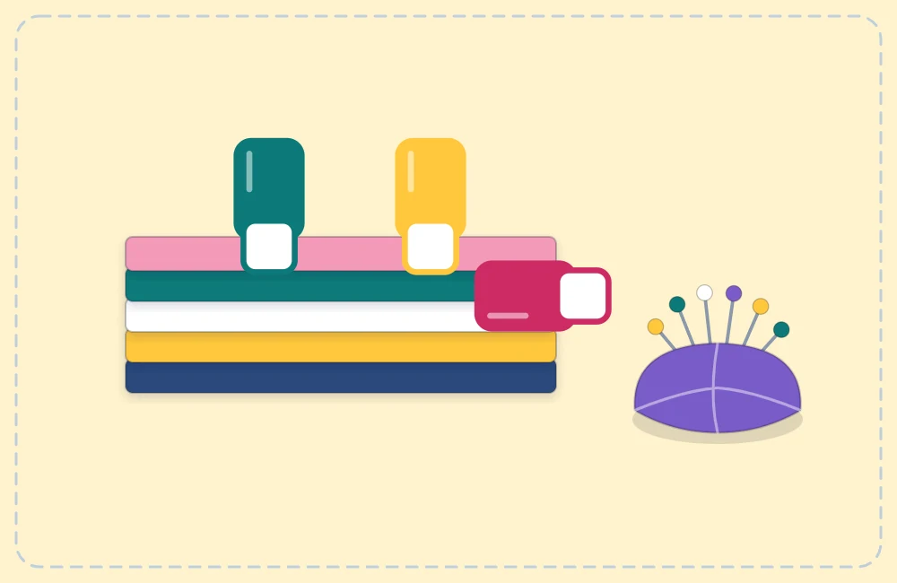 Sewing clips holding a thick stack of fabric layers, with a pincushion beside it